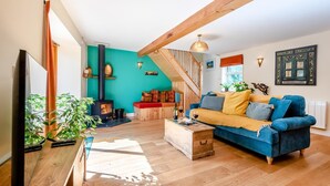 A cozy living room with a wooden floor, a blue sofa, a wooden coffee table, and a fireplace. - 1 Bed in Barnstaple (oc-93422) (Prixford)