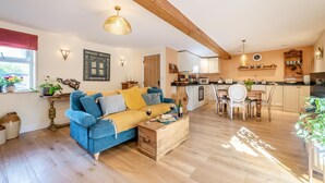 A cozy living room with a blue sofa, wooden coffee table, and a dining area with a white table and chairs. - 1 Bed in Barnstaple (oc-93422) (Prixford)