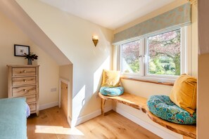 A room with a sloped ceiling, a wooden bench with cushions, a window with a view of trees, and a wooden dresser. - 1 Bed in Barnstaple (oc-93422) (Prixford)