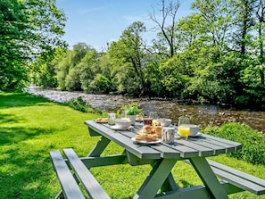 A picnic table set up by a river with food and drinks. - 4 Bed in Ystradgynlais (oc-bn273) (Ystradgynlais)
