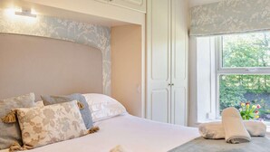Ein Schlafzimmer mit einem großen Bett, einem Kleiderschrank und einem Fenster mit Blick auf Grünflächen.