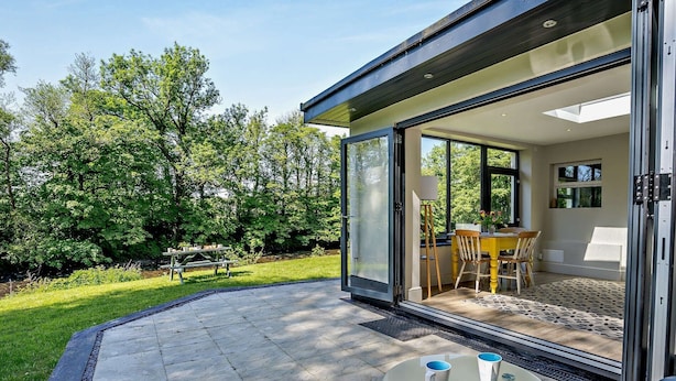 Una casa moderna con una puerta de cristal que da a un patio con mesa y sillas.