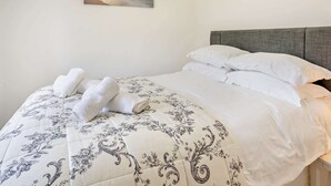 Una cama bien hecha con un edredón estampado con motivos florales, un cabecero gris y un cuadro de una playa en la pared.
