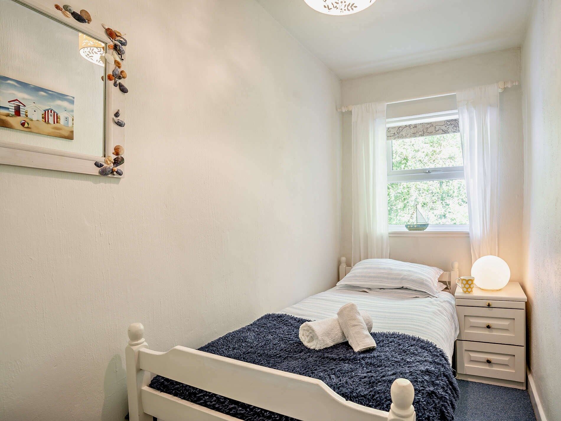 Een slaapkamer met een bed, nachtkastje, lamp en een raam met gordijnen.