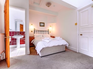 A bedroom with a bed, bedside tables, a wall-mounted light, a picture, and a door.