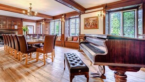 Un vaste espace dédié à la salle à manger, comprenant un piano, des chaises en bois et un banc.
