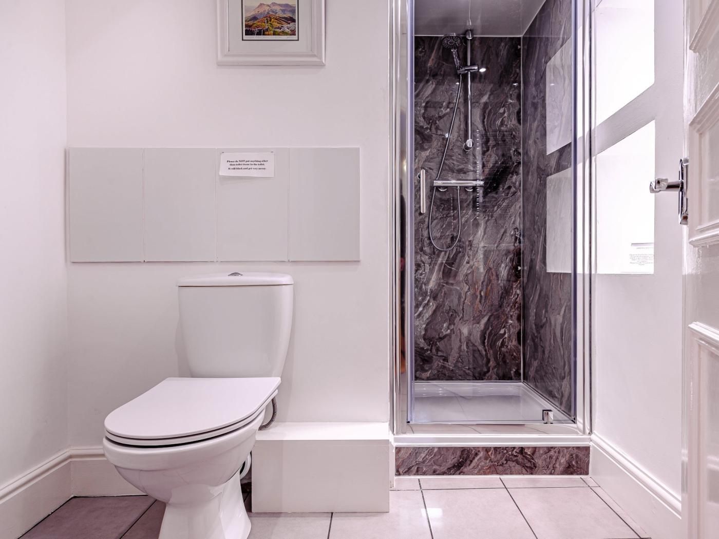 A modern bathroom with a toilet, a shower enclosure, and a marble backsplash.