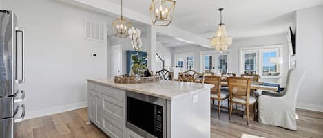 A spacious kitchen with modern appliances, a dining area with wooden chairs, and pendant lighting.