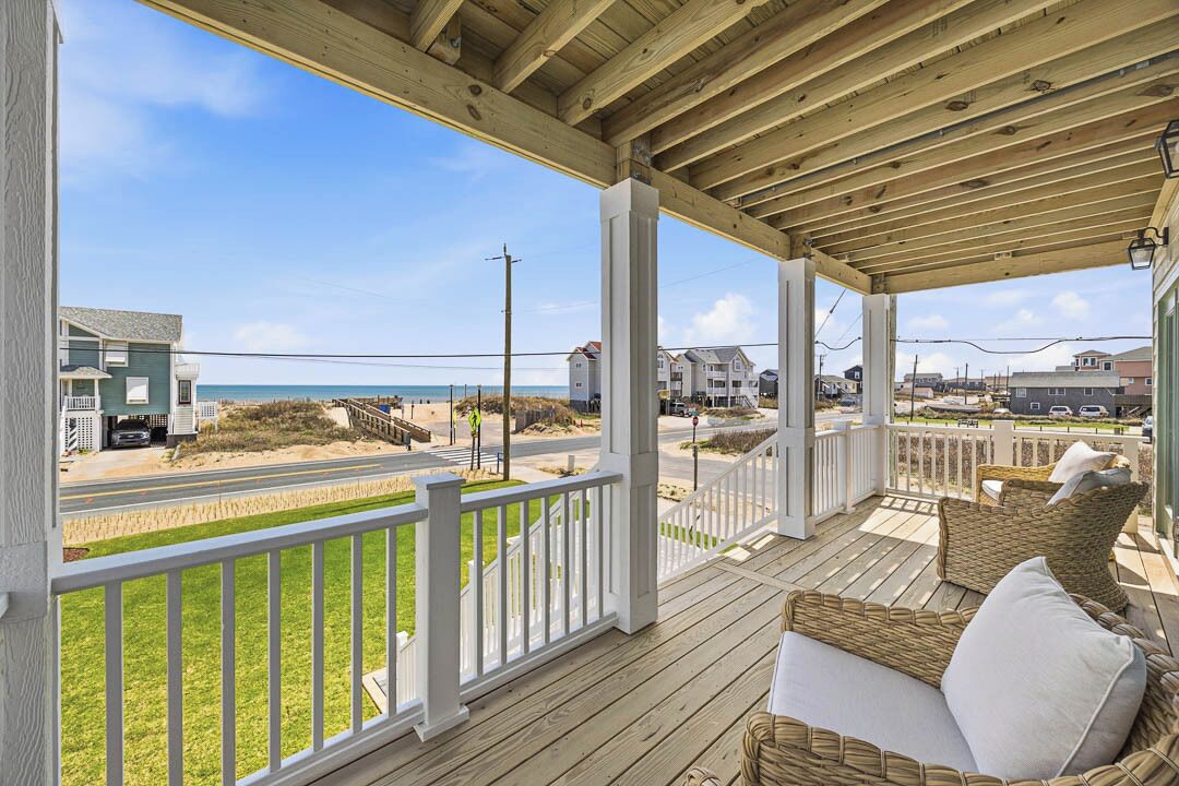 A covered porch with a view of the beach, a wicker sofa, and a railing.