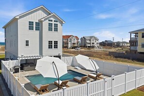 Ett tvåvåningshus med pool, ett vitt staket och utsikt över stranden.