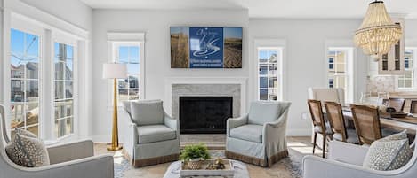 A spacious living room with a fireplace, two armchairs, a coffee table, and a dining area with chairs and a table.