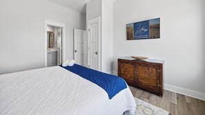 Ein Schlafzimmer mit einem Bett, einem Holzschrank, einem Gemälde und einer Tür zu einem Badezimmer.
