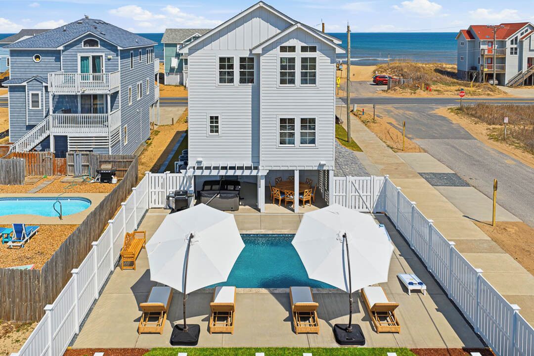 Ein zweistöckiges Haus mit Pool, Sitzgelegenheiten im Freien und Blick auf den Strand.