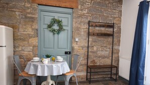 A stone-walled room with a blue door, a small table with chairs, a radiator, and a blue curtain. - 1 Bed in Craster (94372) (Longhoughton)