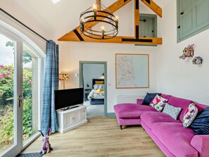 A modern living room with a large window, a pink sofa, a television, and a map on the wall. - 1 Bed in Alnwick (oc-94372) (Longhoughton)