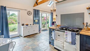 Een moderne keuken met een groot fornuis, een eethoek met een tafel en stoelen, en uitzicht op een tuin door de openslaande deur.