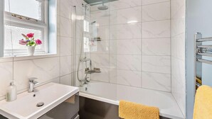 Een badkamer met een douche, een wastafel en een raam met bloemen.