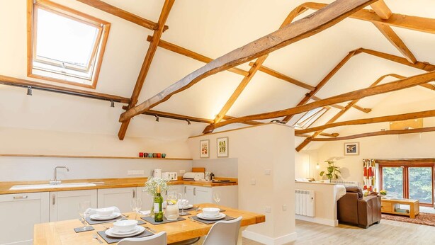 A dining area with a wooden table, chairs, and a kitchen in the background. - 2 Bed in Umberleigh  (88605) (Chittlehampton)