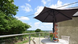 A round wooden table with chairs and a large umbrella on a balcony with a view of the countryside. - 2 Bed in Umberleigh  (88605) (Chittlehampton)