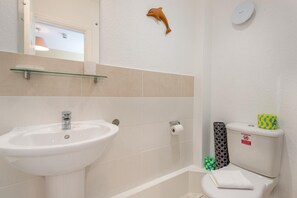 Un baño con lavamanos blanco, inodoro y espejo con repisa de vidrio arriba.