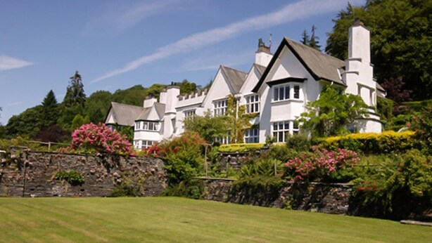 A large, white, multi-story house with a stone wall and lush greenery. - 2 Bed in Hawkshead (oc-llh12) (Claife)