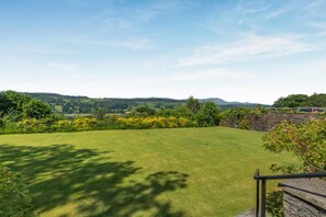 A well-maintained lawn with a stone wall and a metal railing, overlooking a hilly landscape with trees and a clear sky. - 2 Bed in Hawkshead (oc-llh12) (Claife)