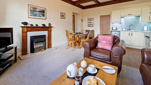 A living room with a fireplace, a dining area, a kitchen, and a brown leather sofa. - 2 Bed in Hawkshead (oc-llh12) (Claife)