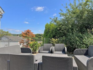 Terrassenbereich mit Korbmöbeln im Freien und Blick auf Bäume sowie ein Gebäude im Hintergrund.