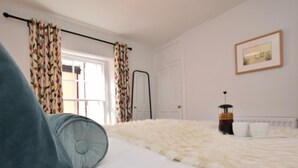 Ein Schlafzimmer mit einer flauschigen weißen Bettdecke, einem Heizkörper, einem gerahmten Bild an der Wand und Vorhängen mit Blumenmuster.