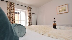 A bedroom with a bed, a radiator, a window with curtains, and a framed picture on the wall.