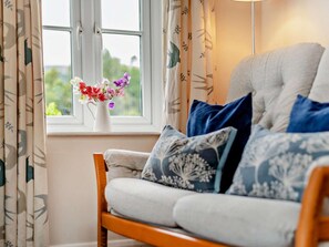 Ein Zimmer mit einer Couch, einer Blumenvase und einem Fenster mit Vorhängen.