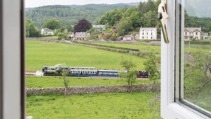 Une vue pittoresque d’un train traversant un paysage rural, avec des maisons et de la végétation.