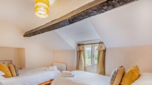 Une chambre avec deux lits, une fenêtre avec des rideaux, un radiateur et un plafond avec une poutre en bois.