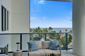 Ein Balkon mit einer Couch, einem kleinen Tisch und Blick auf das Meer und Palmen.