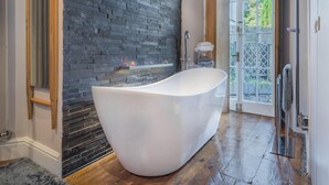 A modern bathroom with a freestanding bathtub, a stone wall, and a view through a glass door. - 1 Bed in Coniston Lake (SZ402) (Blawith)