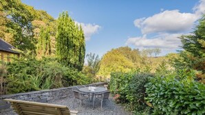 A garden patio with a wooden bench and a table, surrounded by dense greenery and trees. - 1 Bed in Coniston Lake (SZ402) (Blawith)