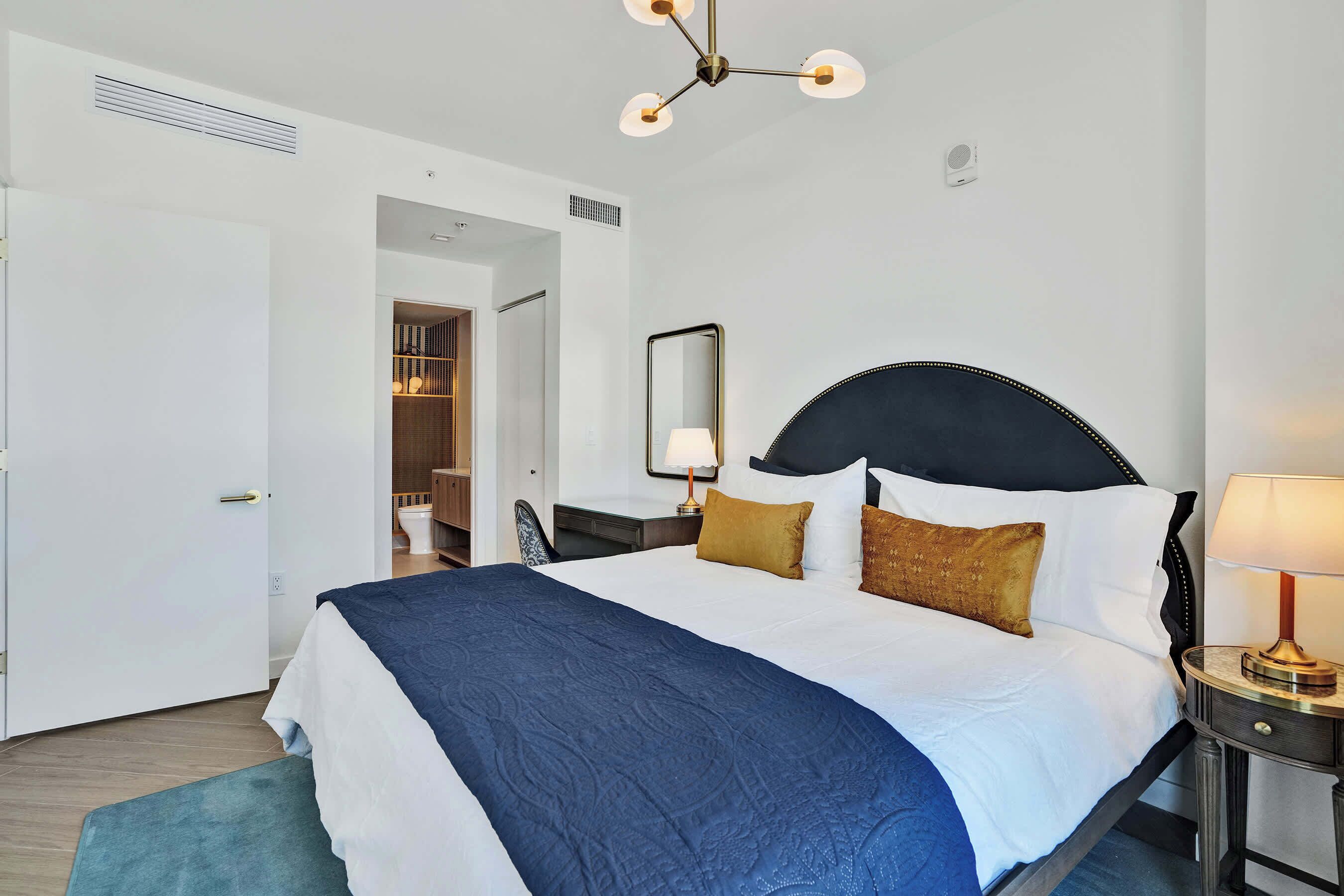 A hotel room with a bed, bedside lamps, a mirror, and a wardrobe.