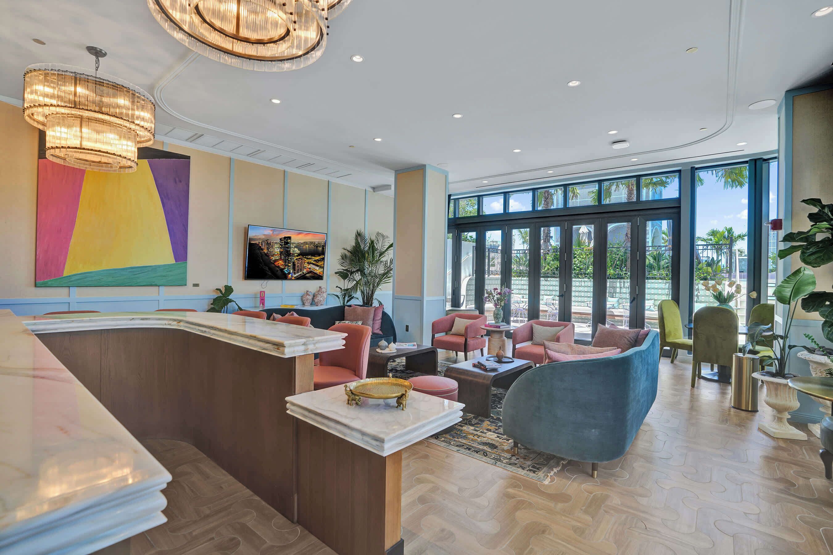 A modern hotel lobby with a reception desk, seating area, large windows, and a colorful wall art piece.