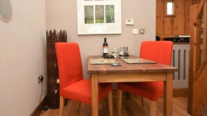 Un coin repas avec une table en bois, deux chaises rouges, une bouteille de vin et une fenêtre.