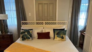 A bedroom with a bed, a headboard, a bedside table, a lamp, and a patterned rug. - Entire rental, Adama Suites St John’s Antigua (Potters Village)