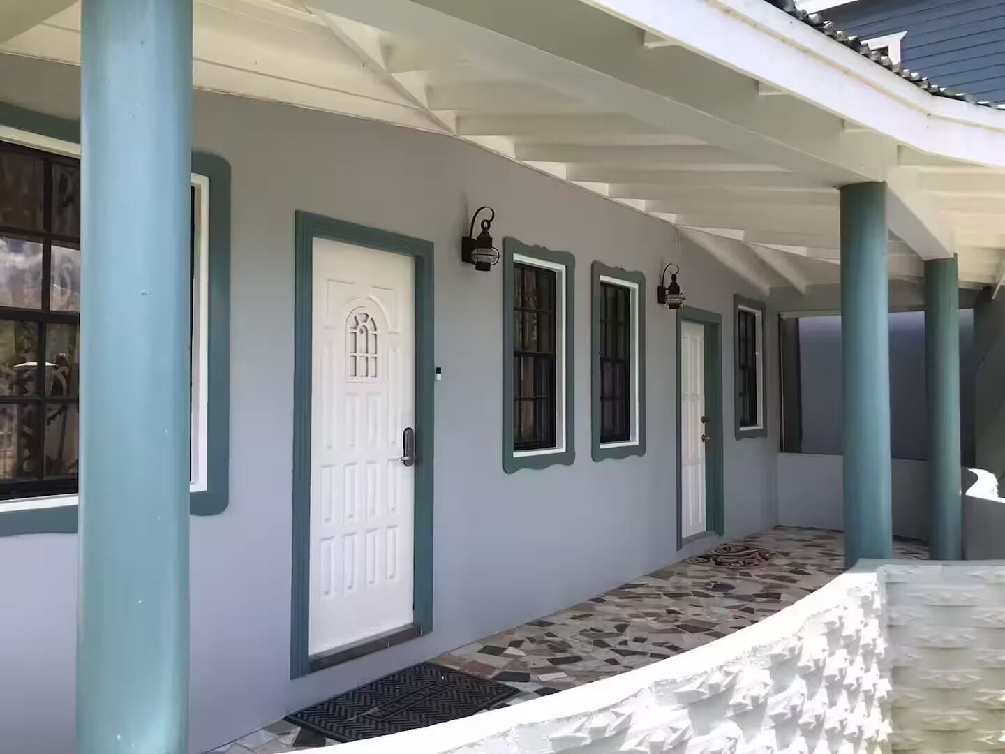 Un pasillo cubierto con varias puertas y ventanas, un piso con diseño y una barandilla metálica.