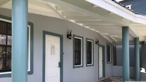 A covered walkway with a series of doors and windows, a patterned floor, and a metal railing. - Entire rental, Adama Suites St John’s Antigua (Potters Village)