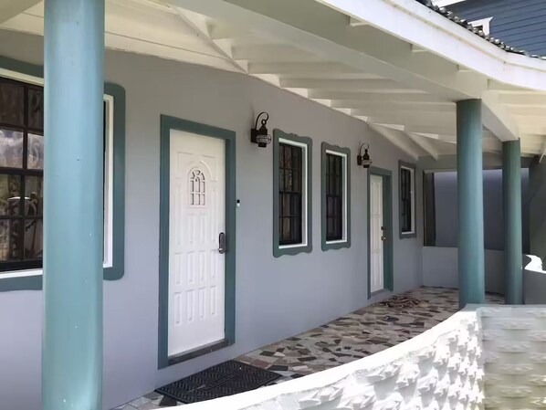 A covered walkway with a series of doors and windows, a patterned floor, and a metal railing.
