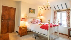 Une chambre à coucher avec un lit, des tables de chevet, une commode, une fenêtre avec des rideaux, une porte en bois et un tableau au mur.