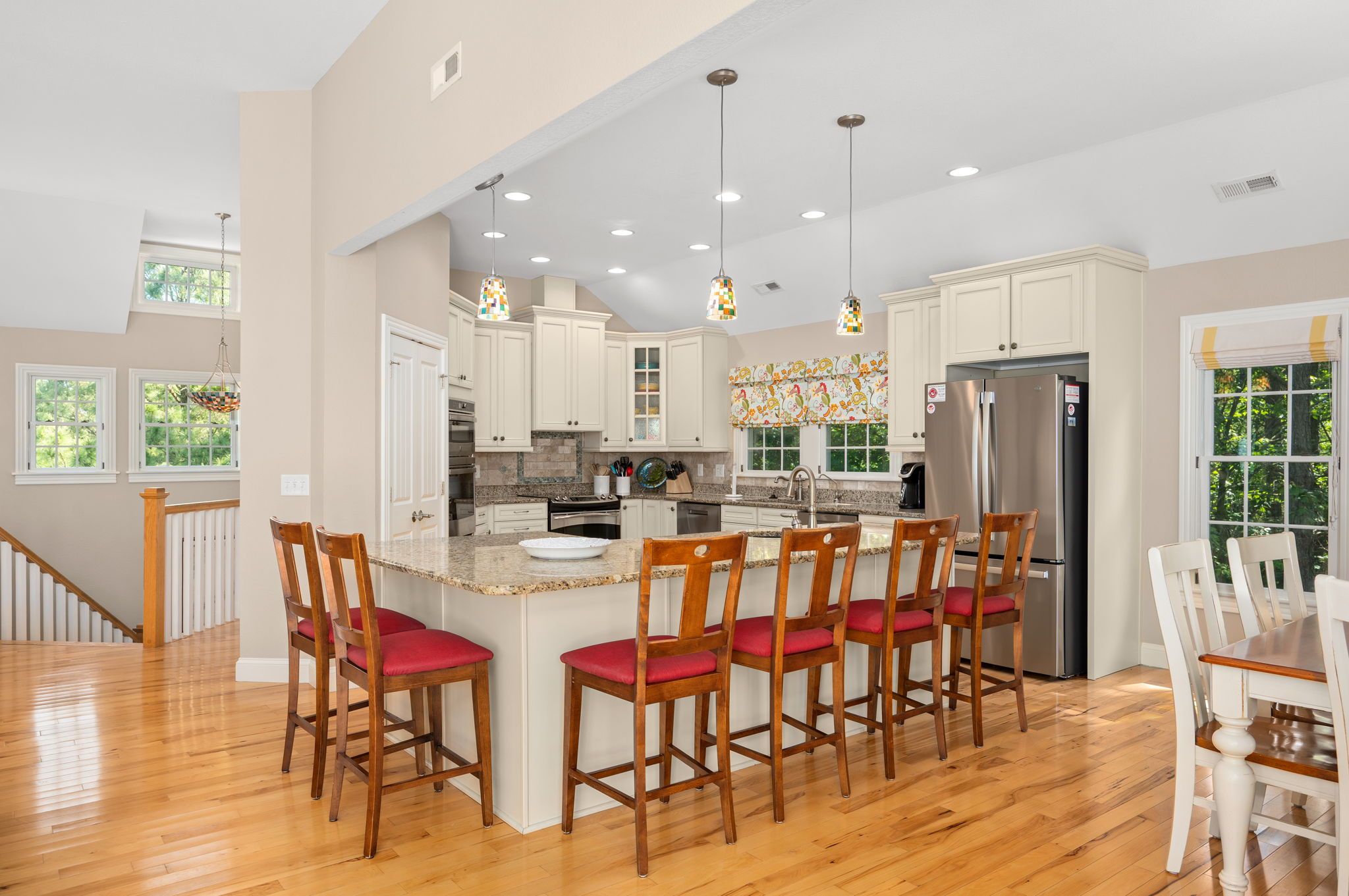 A spacious kitchen with a central island, wooden chairs, and a stainless steel refrigerator.