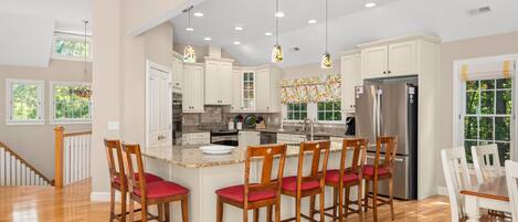 A spacious kitchen with a central island, wooden chairs, and a stainless steel refrigerator.