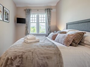 Ein Schlafzimmer mit einem Bett, Kissen, einem Fernseher und einem Fenster mit Vorhängen.