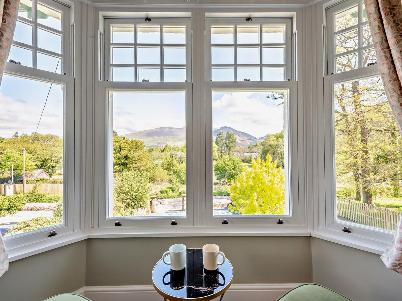 A room with a bay window overlooking a landscape with trees and hills.