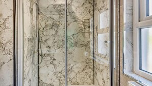 Ein Badezimmer mit einer Duschkabine aus Glas, Marmorwänden und einem Fenster.