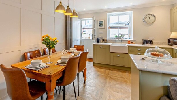 A modern kitchen with a dining area, wooden table, chairs, pendant lights, and a view through the window. - 2 Bed in Keswick (oc-93224) (Keswick)